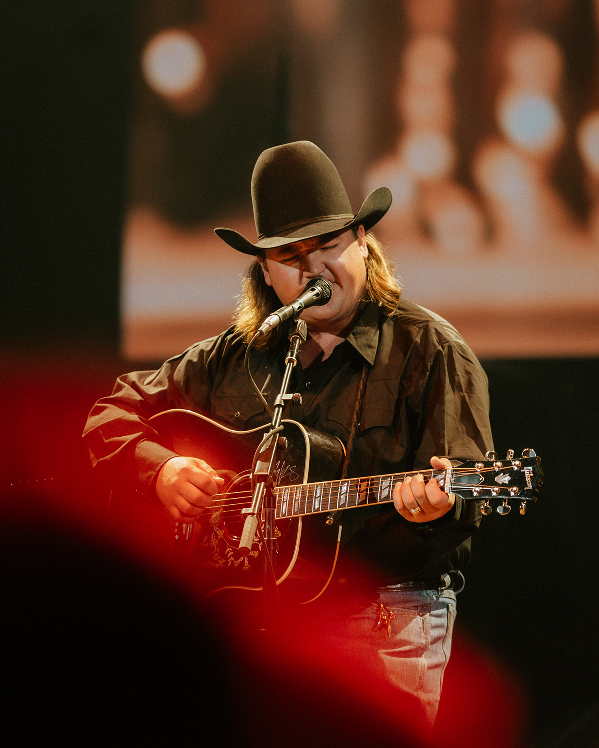 Jake Gardner sings onto a microphone while holding a guitar